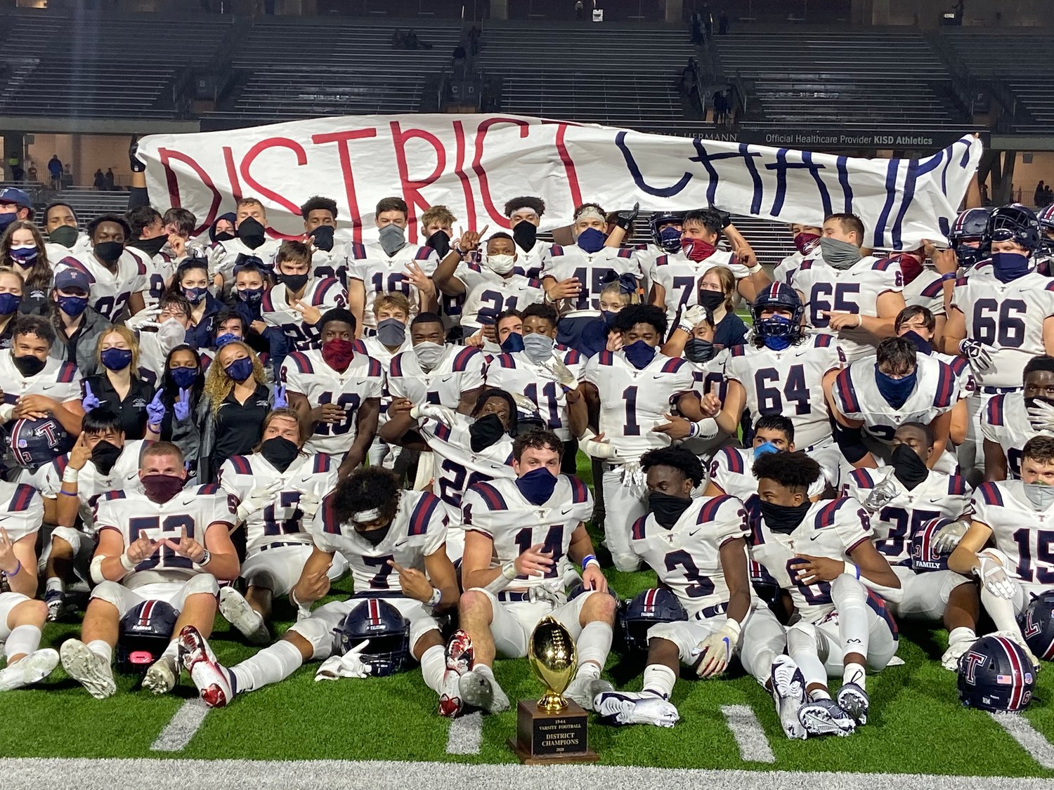 Tompkins players celebrate with a 'District Champs' banner and the 19-6A district championship trophy following their win over Seven Lakes on Nov. 27.